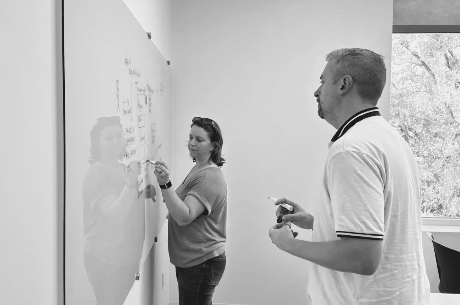 Two of Openlane's founders working at a glass whiteboard, one sketching a diagram while the other holds a marker.