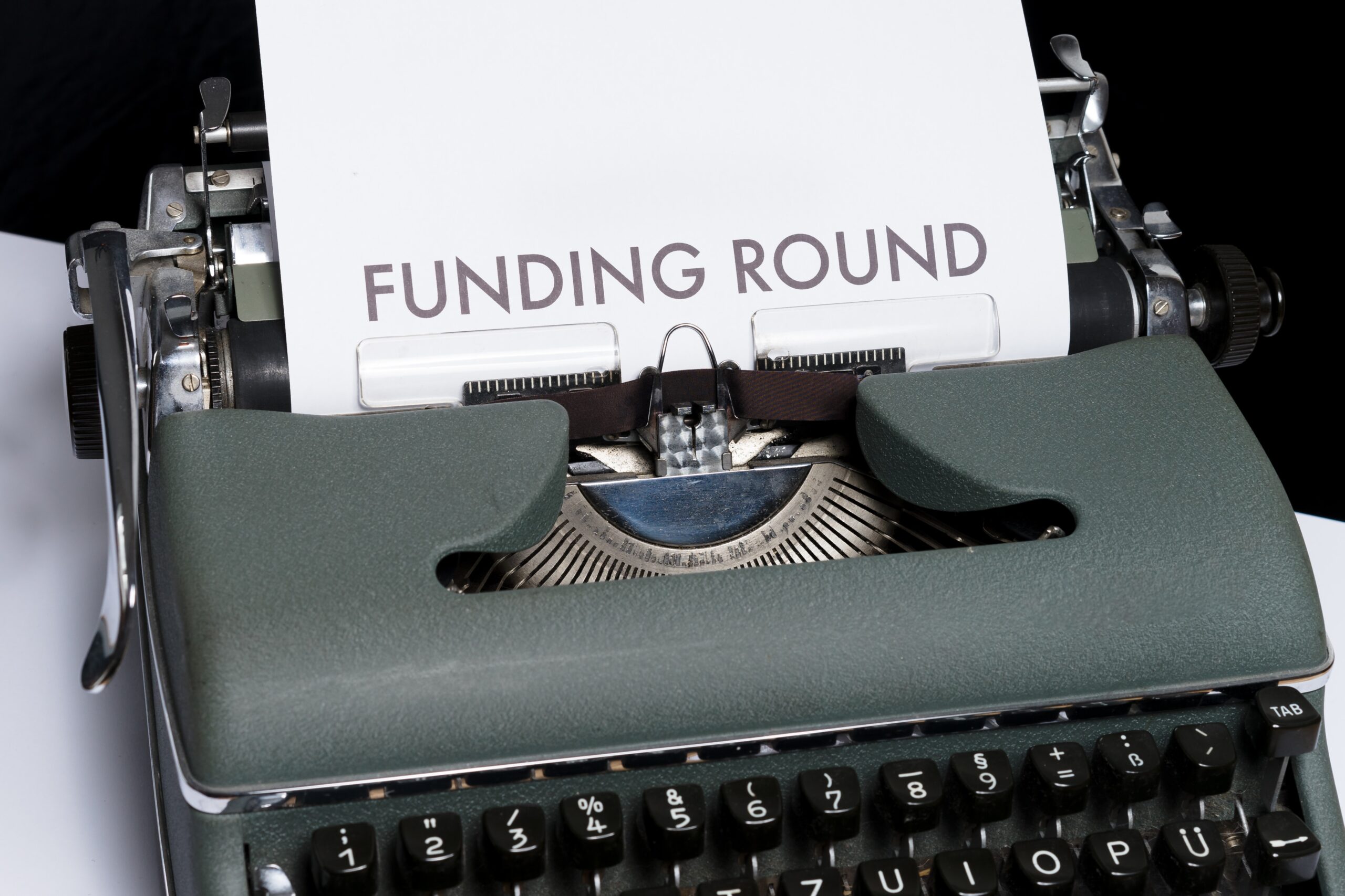 The image shows a typewriter with paper in it that says "Funding Round"