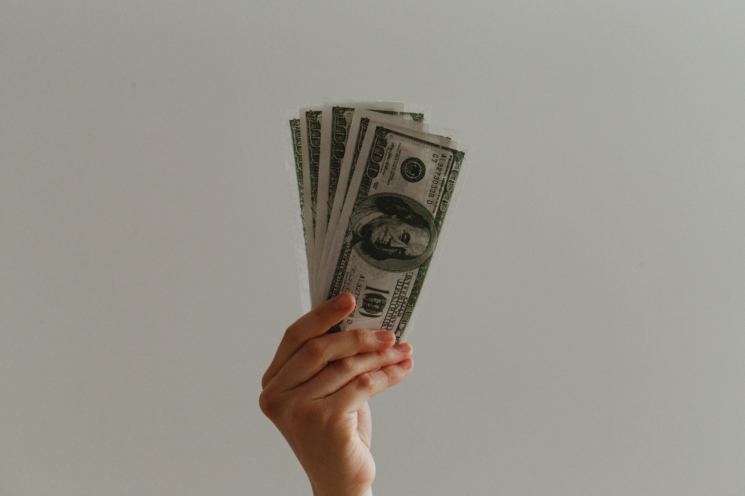 An image of a hand holding up hundred dollar bills. Photo by Jp Valery on Unsplash.